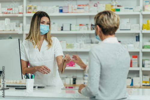Pharmacist wearing protective mask and serving a customer patient in a pharmacy