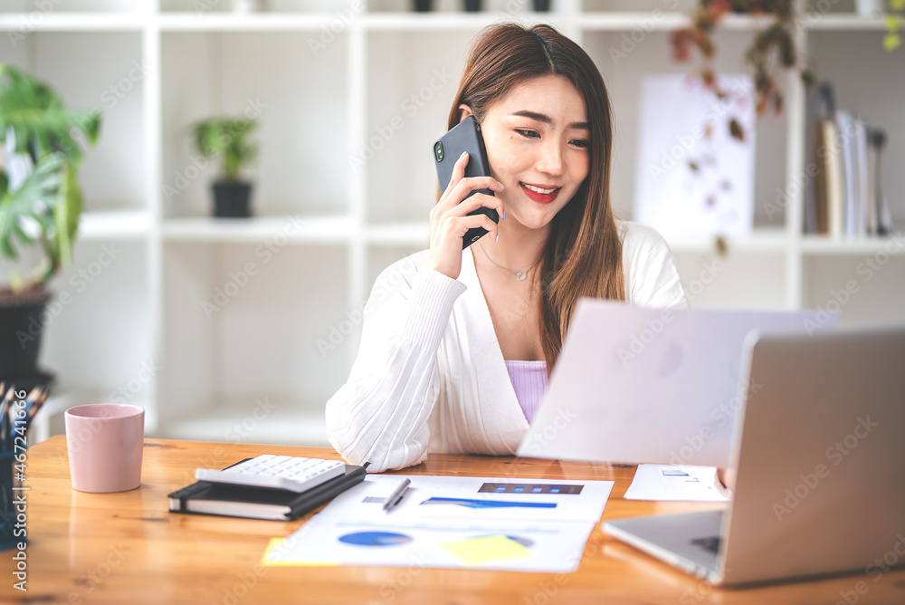 Businesswoman or accountant using the phone to check business information. Accounting Documents and Laptop at Small Office Business Ideas Businesswoman or accountant using the phone to check business information. Accounting Documents and Laptop at Small Office Business Ideas