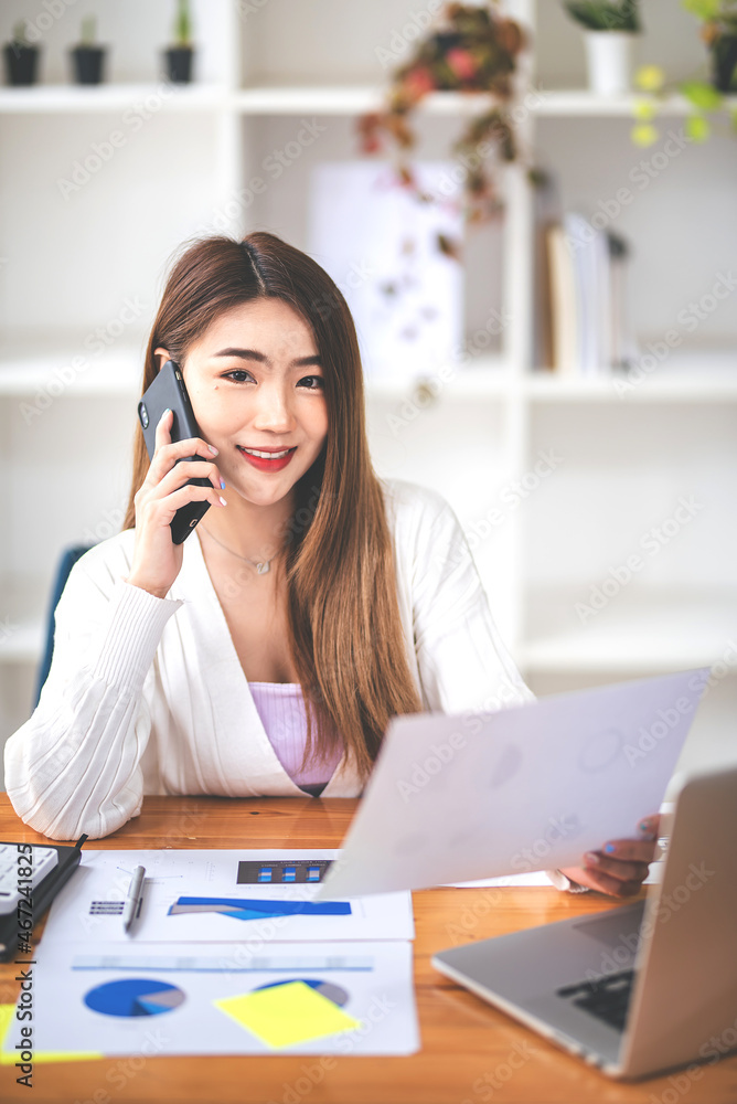 Businesswoman or accountant using the phone to check business information. Accounting Documents and Laptop at Small Office Business Ideas Businesswoman or accountant using the phone to check business information. Accounting Documents and Laptop at Small Office Business Ideas