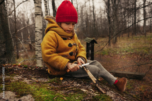 Little Girl Sitting in the Forest and Planing a Stick With a Knife photo