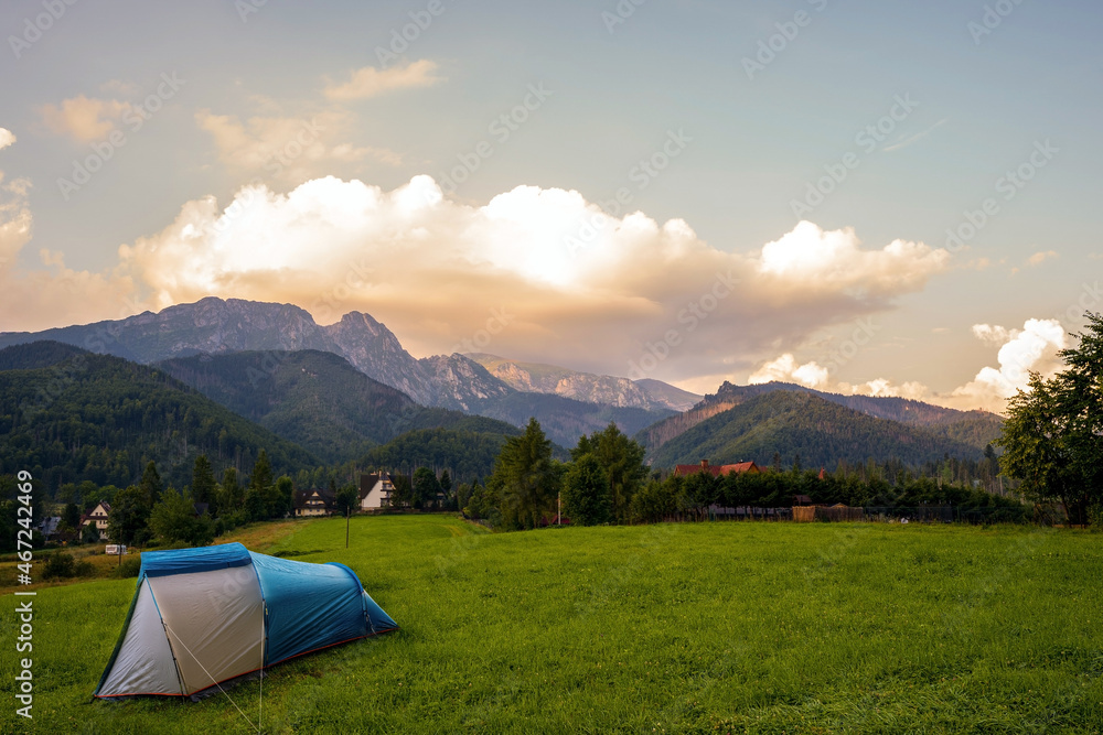Camping tent put up on green grass meadow field against tatra mountains landscape during sunset sunrise and dramatic clouds, adventure in wild nature concept.
