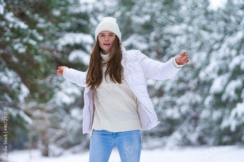 Close up portrait of happy girl in jacket  enjoying winter moments. Outdoors photo of a long-haired laughing lady in a knitted hat having fun on a snowy morning on a blurred background of wood