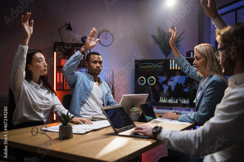 Group of male and female creative colleagues holding one arm raised while voting at office room. Four diverse partners unanimously supporting new strategy of common business project. photo