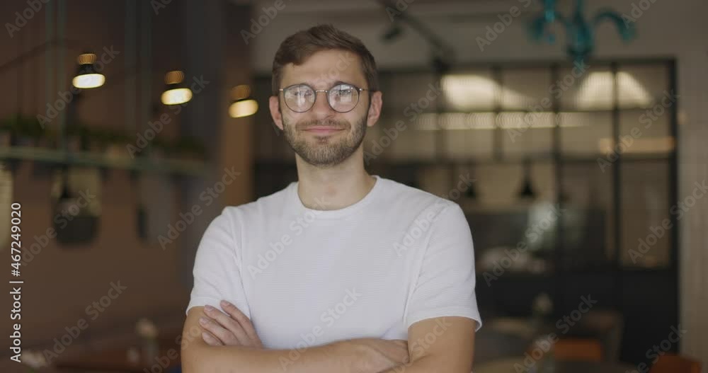 Smiling man in glasses standing in cafe indoors crossing hands in slow motion looking at camera. Portrait of positive confident handsome businessman owner Smiling man in glasses standing in cafe indoors crossing hands in slow motion looking at camera. Portrait of positive confident handsome businessman owner