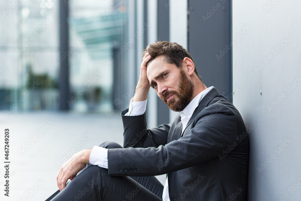 Sad depressed entrepreneur in formal suit worker man sitting near outdoors street near modern office business center. Upset male businessman lost job due financial crisis employee has problem. outside Sad depressed entrepreneur in formal suit worker man sitting near outdoors street near modern office business center. Upset male businessman lost job due financial crisis employee has problem. outside