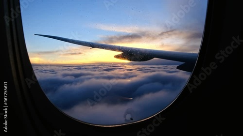 View through dirty fogged airplane window onto wing at sunset. plane flies into clouds at dusk or dawn and prepares for landing, cinematic view of clouds with golden sun.