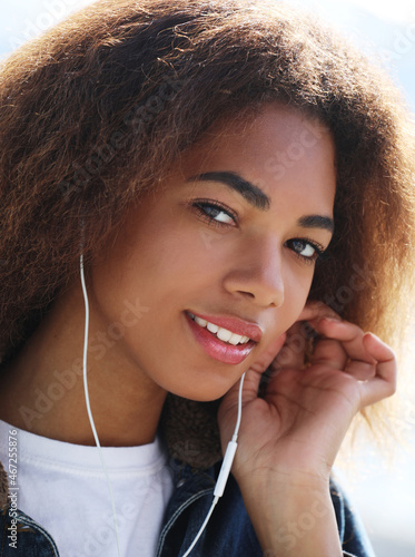 lifestyle concept: Young african american girl using mobile phone and headphones, smiling,