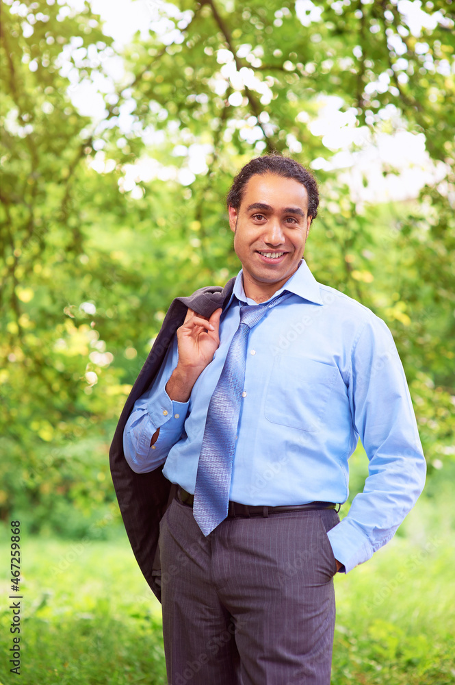 Happy relieved businessman stands in park with his jacket over his shoulder. Happy relieved businessman stands in park with his jacket over his shoulder.