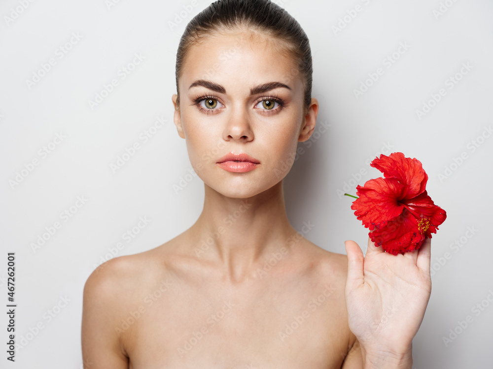 woman holding a red flower in her hand on a light background naked shoulders woman holding a red flower in her hand on a light background naked shoulders