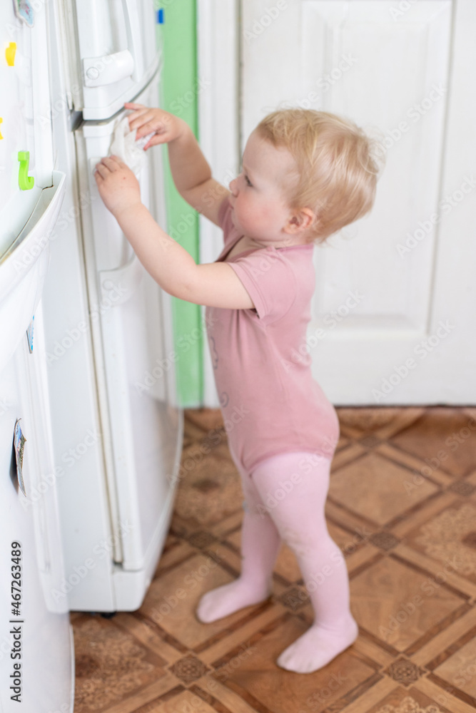 A toddler washes the refrigerator with wet wipe tissue during a viral epidemic. Cleaning home. Teaching children to be independent. use of wet wipes in everyday life A toddler washes the refrigerator with wet wipe tissue during a viral epidemic. Cleaning home. Teaching children to be independent. use of wet wipes in everyday life