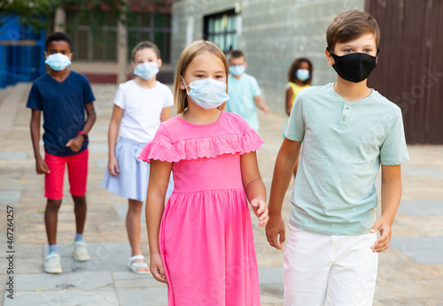 Tween girl and boy enjoying walk together through city in warm summer day. Children wearing protective masks to prevent spread of viral infections