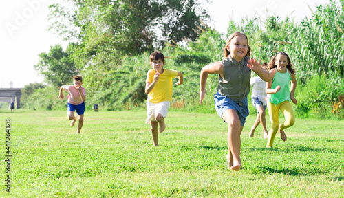 Group of school children, boys and girls, laughing and running in a city park at summer day