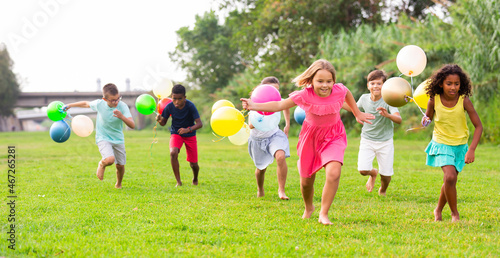 Group of happy kids running through grass with balloons in hands. © JackF