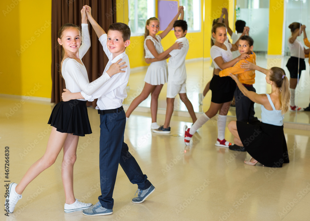 Pairs of kids are dancing waltz in class.