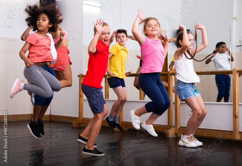 Cheerful preteen boys and girls having fun in group dance class, jumping with female coach