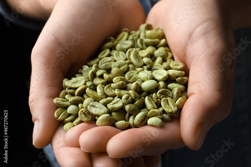 Woman holding pile of green coffee beans on black background, closeup © New Africa