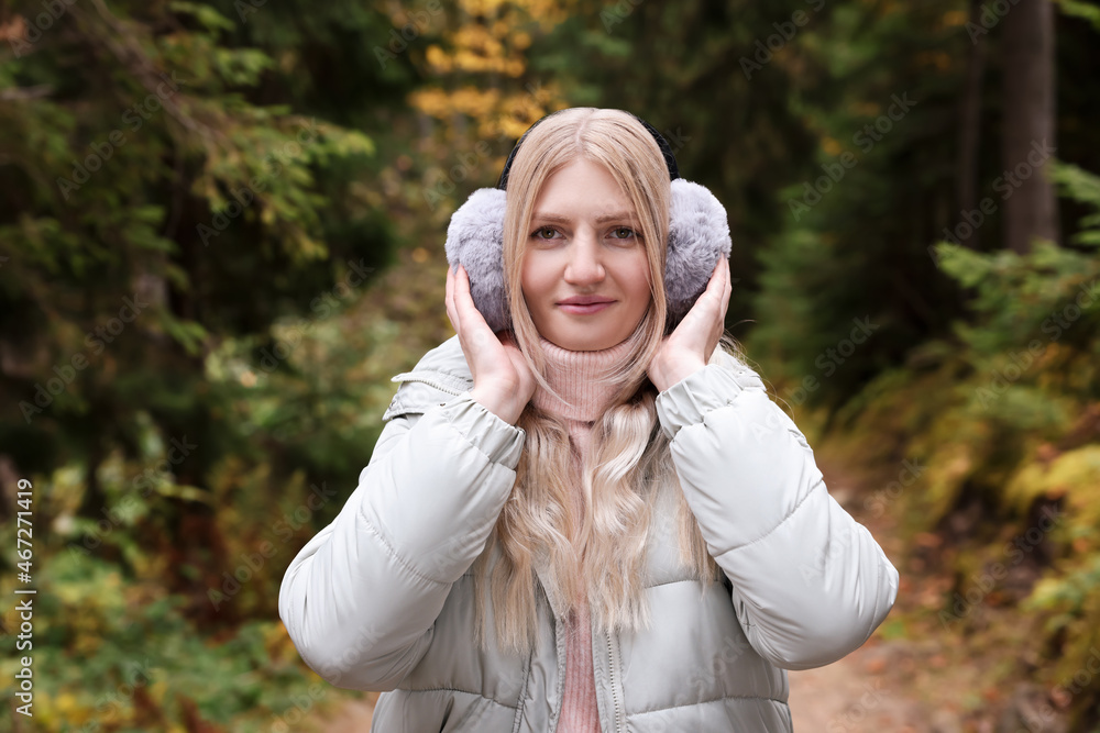 Young beautiful woman wearing warm earmuffs in forest Young beautiful woman wearing warm earmuffs in forest
