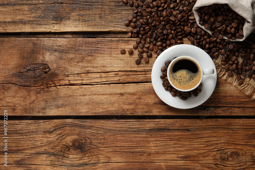 Cup of aromatic hot coffee and beans on wooden table, flat lay. Space for text Cup of aromatic hot coffee and beans on wooden table, flat lay. Space for text
