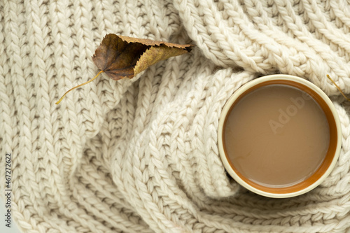 Cup of autumn coffee, tea or hot chocolate, fall leaf on a warm scarf. Drink for autumn cold rainy days. Sunday relaxing, Hygge, still life concept. Flat lay, top view, copy space.
