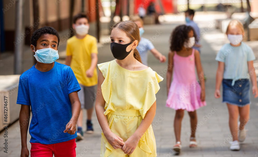 Group of children in protective medical masks walking on city street in fine weather