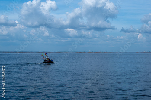 A small boat floated in the sea, the sky was blue with white clouds.
