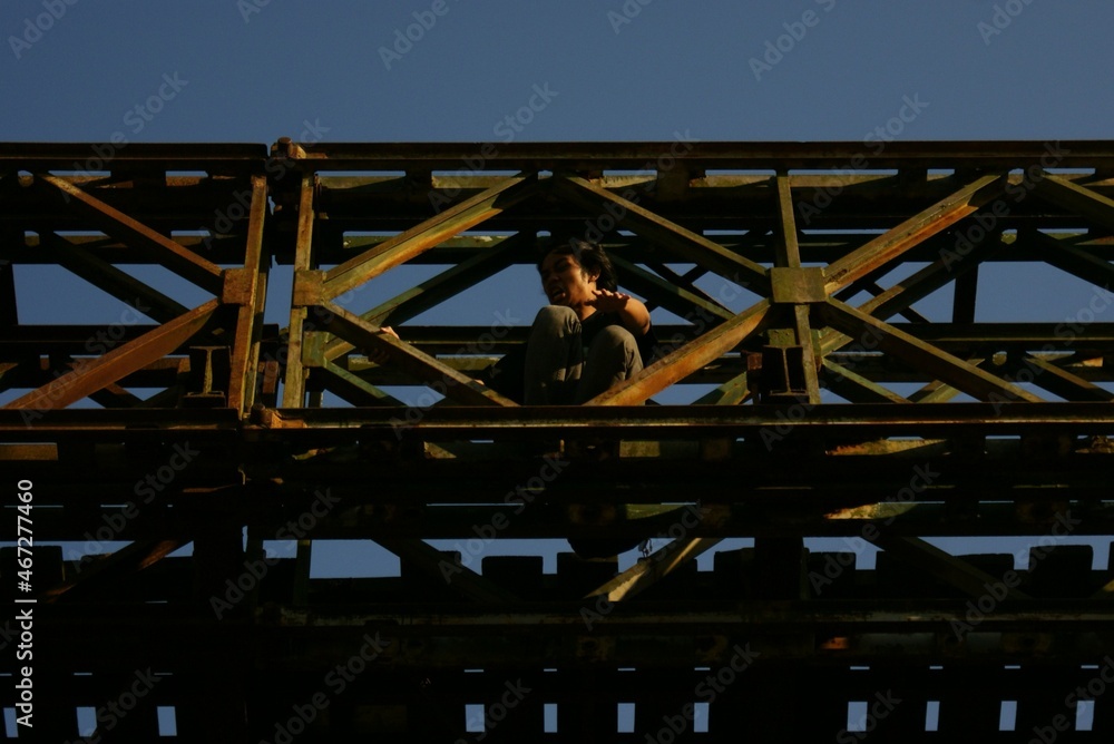 A man with long hair playing and posing on an old bridge against a blue sky