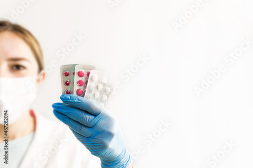 Hands in medical blue gloves are holding pills, and in the background a woman wearing a medical mask is out of focus. Selective focus. drugstore sale concept. Medicines and pills.banner for pharmacy.

