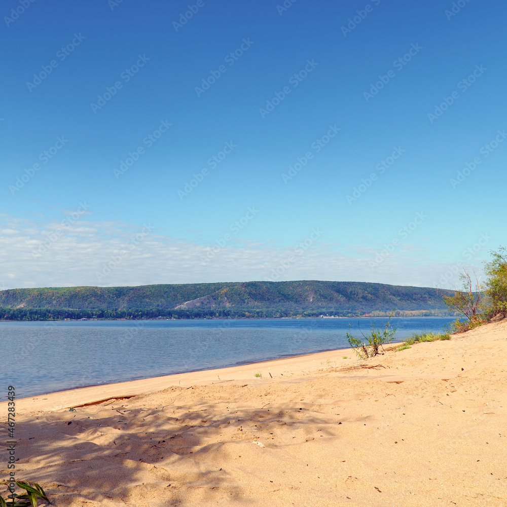 The sandy shore of the big Volga river against the background of blue cloudy sky. On the opposite bank of the Zhiguli Mountains