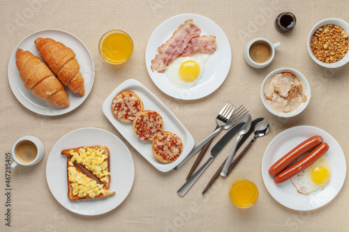 Hearty homemade family breakfast. Eggs, bacon, sausages, beans, croissants, toast and coffee on the table. Top View