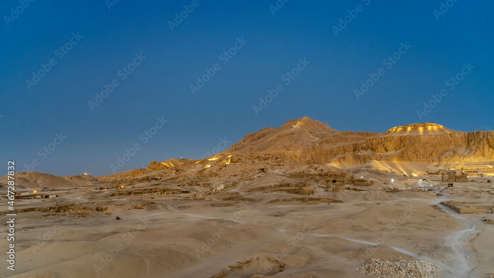 Picturesque rocks stand out against the blue evening sky. In the distance is the temple of Queen Hatshepsut. In the foreground is a sandy desert with archaeological excavations. Luxor. Egypt Picturesque rocks stand out against the blue evening sky. In the distance is the temple of Queen Hatshepsut. In the foreground is a sandy desert with archaeological excavations. Luxor. Egypt
