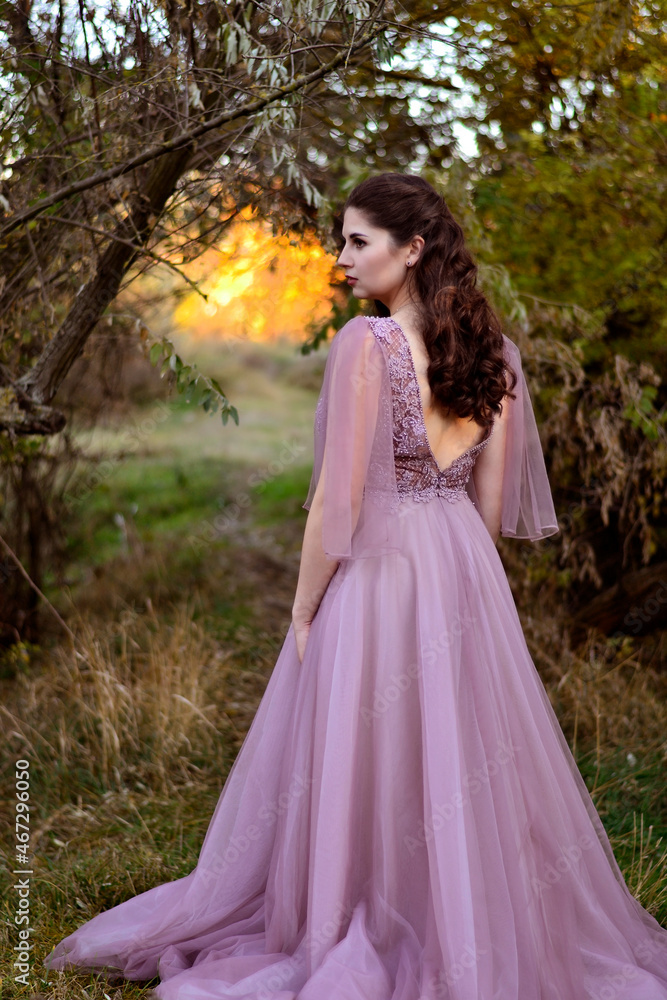 A young long-haired brown-haired woman in a long pink dress in a clearing