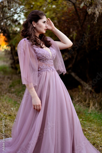 A young long-haired brown-haired woman in a long pink dress in a clearing