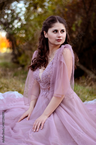 A young long-haired brown-haired woman in a long pink dress in a clearing