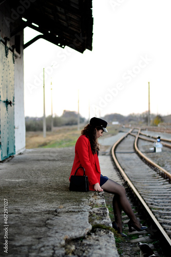 A young long-haired brown-haired woman in a black beret and a red coat on the station platform