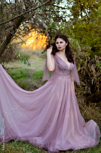 A young long-haired brown-haired woman in a long pink dress in a clearing