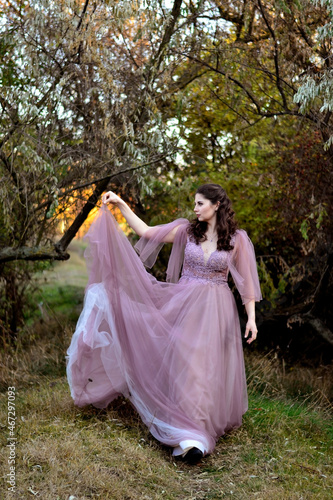 A young long-haired brown-haired woman in a long pink dress in a clearing