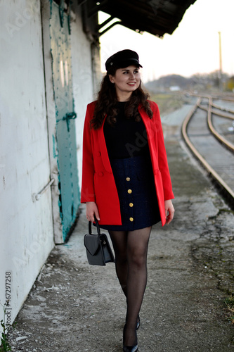 A young long-haired brown-haired woman in a black beret and a red coat on the station platform