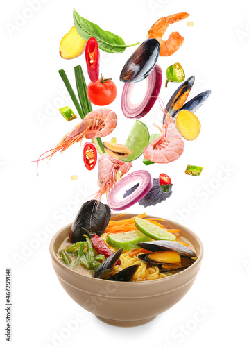 Bowl of tasty Thai soup with flying ingredients on white background
