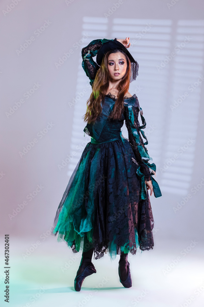 Classical Ballet Ideas. Professional Japanese Female Ballet Dancer In Flying Bat Costume Posing in Dance Pose On Pointeshoes With Lifted Hand and Pattern Against White