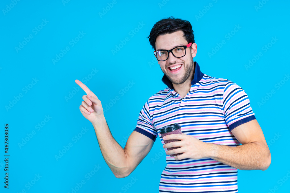 Positive Smiling Caucasian Handsome Brunet Man With Brown Paper Cup While Posing in Glasses Gesturing With Point Finger Against Blue Background. Positive Smiling Caucasian Handsome Brunet Man With Brown Paper Cup While Posing in Glasses Gesturing With Point Finger Against Blue Background.