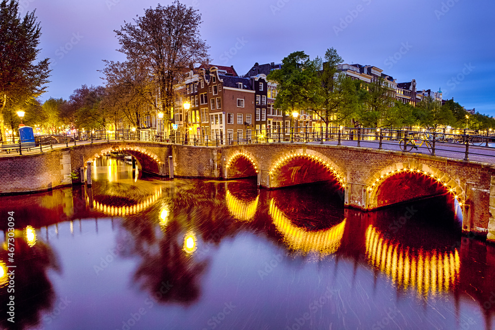European Heritage. Night View of Picturesque  Amterdam Cityscape with One of Its Canals. With Illuminated Bridge and Traditional Dutch Houses At Twilight on Background in Amsterdam.