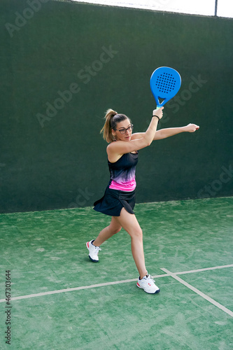 Woman playing paddle tennis, hitting the ball forehand, coming off the wall.  © JoseIMartin