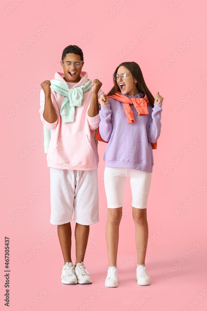 Emotional stylish young couple in hoodies on pink background Emotional stylish young couple in hoodies on pink background