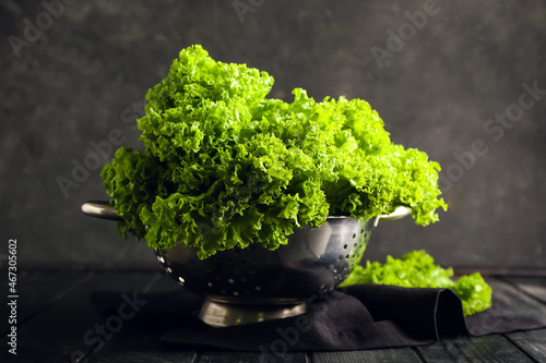 Quadro su tela Colander with fresh lettuce on dark background