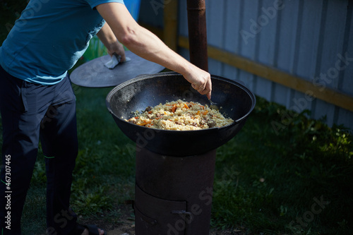 Foto A man is stirring food cooked pilaf outdoors in a cauldron on an open fire , Asi