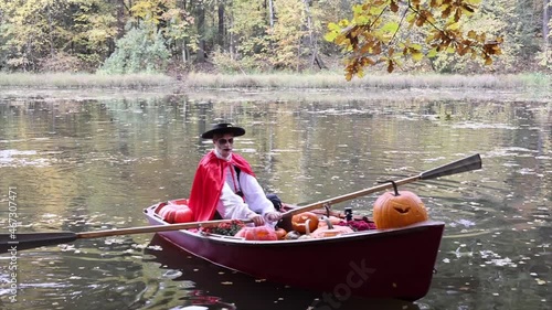 young man dressed as gondolier in gondola boat decorated with pumpkins on pond in autumn park celebrates Halloween and having fun, concept of Halloween carnival or costume party