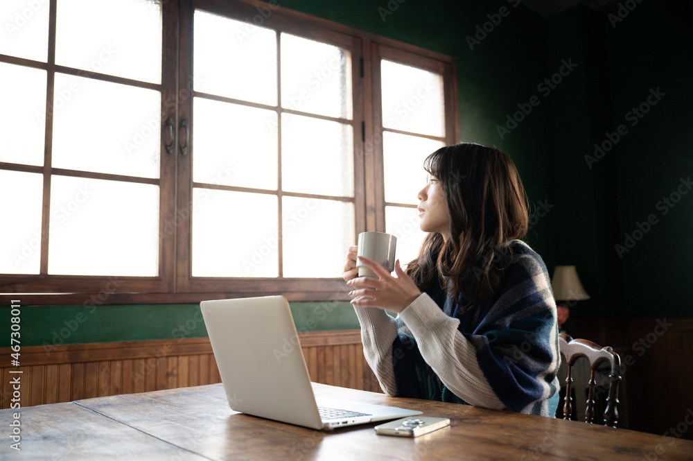 An Asian (Japanese) woman stares at the window while holding a cup of coffee wide angle An Asian (Japanese) woman stares at the window while holding a cup of coffee wide angle