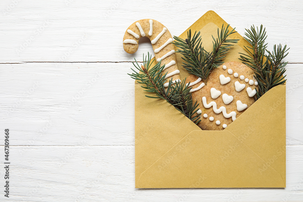 Envelope with fir tree branches and cookies on white wooden background