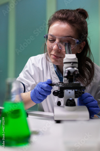 Portrait of botanist researcher woman analyzing gmo leaf sample under microscope searching for genetically modified plant. Biologist scientist working in microbiology hospital laboratory