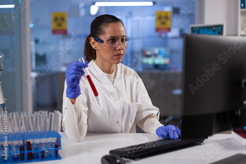 Specialist researcher woman typing biomedical expertise on computer after analyzing test tubes with patient blood during microbiology laboratory. Chemist doctor working in pharmacy laboratory